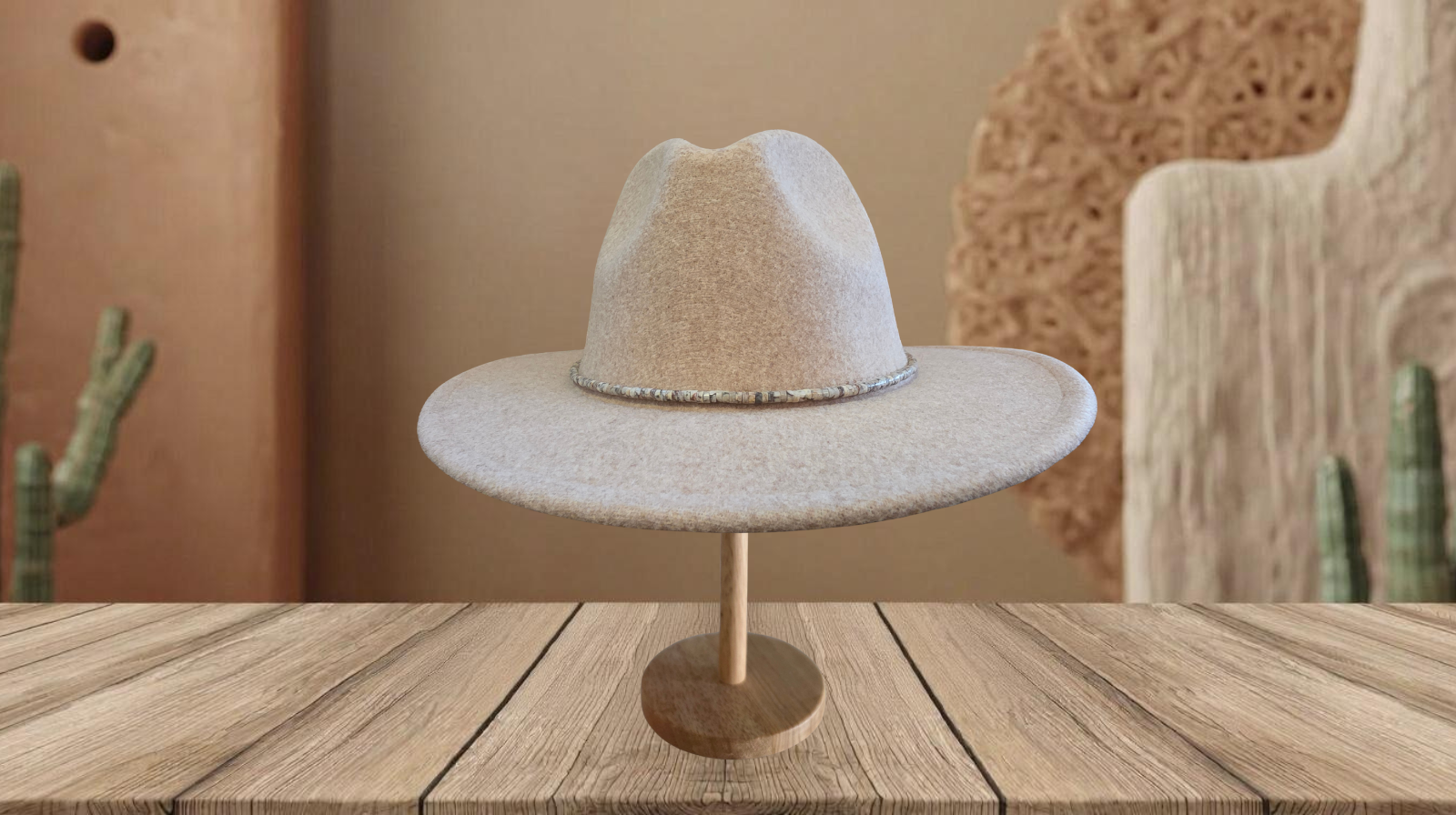 A light beige wide-brim fedora hat displayed on a wooden stand, set against a rustic desert-themed background with a wooden table, cacti, and textured decor.