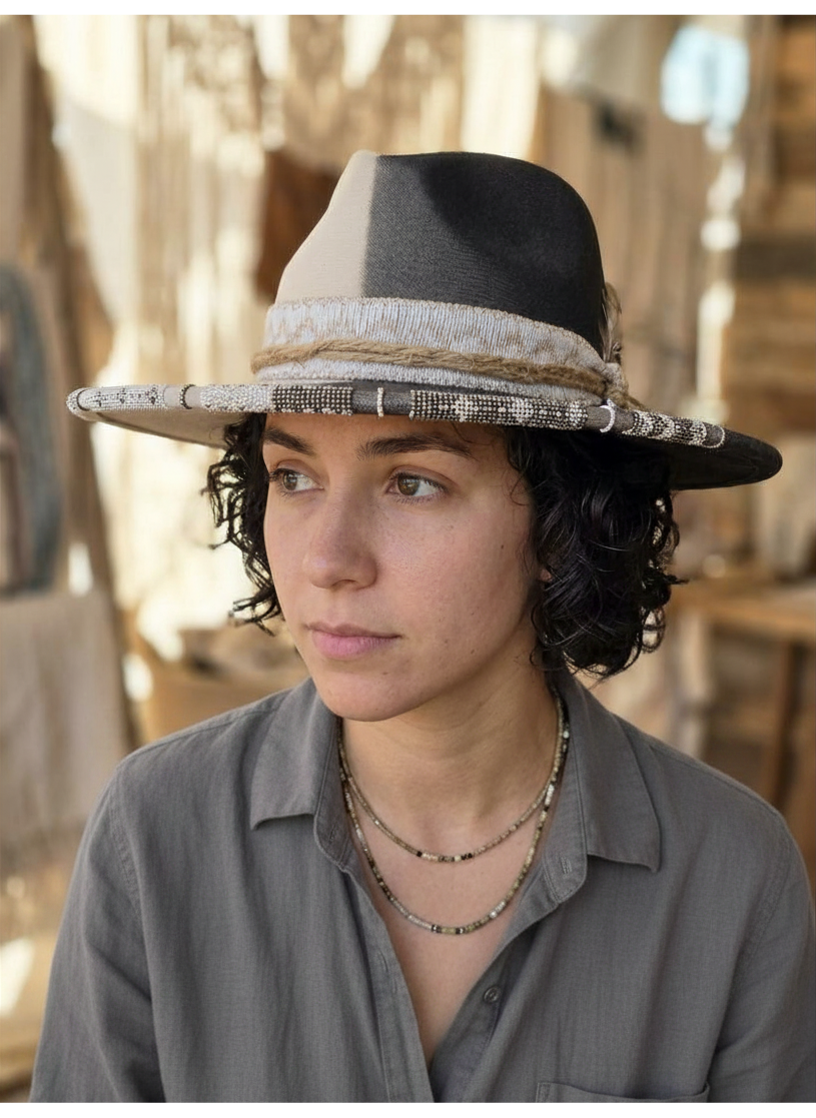 A person wearing a two-tone beige and black wool fedora hat featuring an intricately hand-beaded brim.
